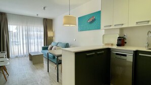 A modern kitchen with a dishwasher, a sink, and a countertop. There is a dining table with chairs and a sofa in the living area.