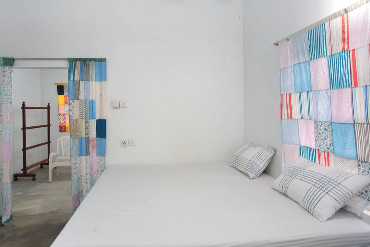 Une chambre à coucher avec un lit, des oreillers, une chaise en bois et un rideau matelassé.