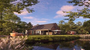 A modern house with a pond, surrounded by trees and a clear sky.