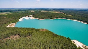 An aerial view of a large turquoise lake surrounded by dense forest, with a small beach area and distant fields. - Private relaxation retreat for a family (TA Gasselte)