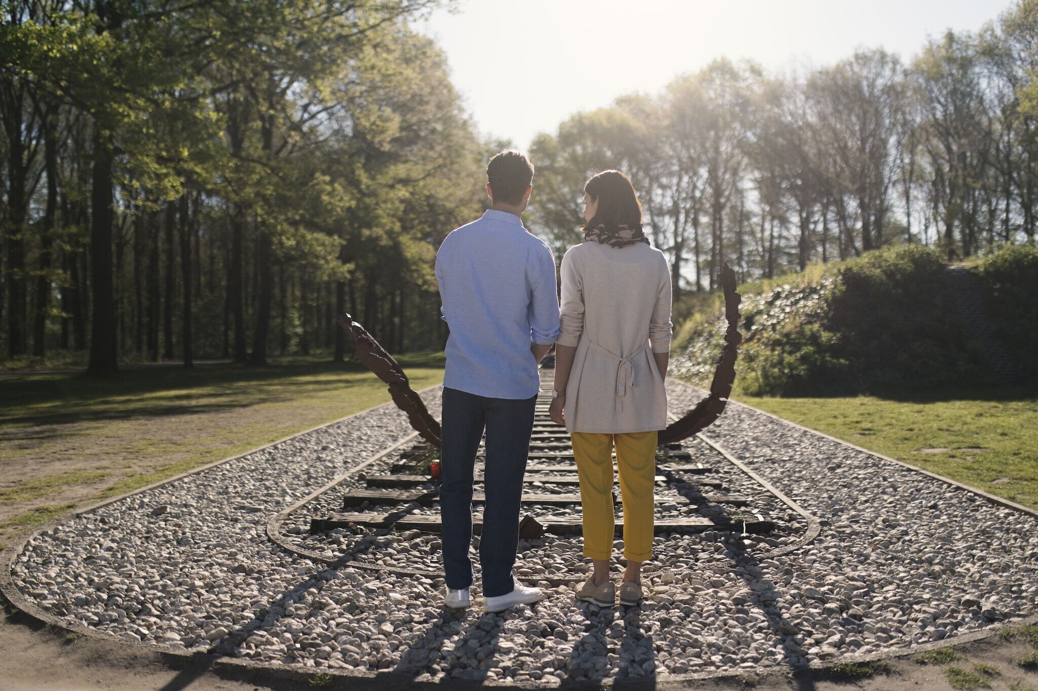 Two people standing on a gravel path with a circular stone design, surrounded by trees.