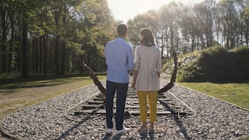 Two people standing on a gravel path with a circular stone design, surrounded by trees.