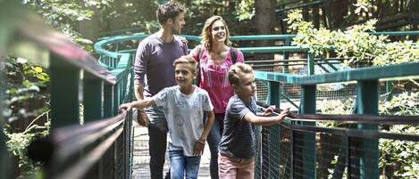 A family walking on a wooden bridge with metal railings, surrounded by greenery.