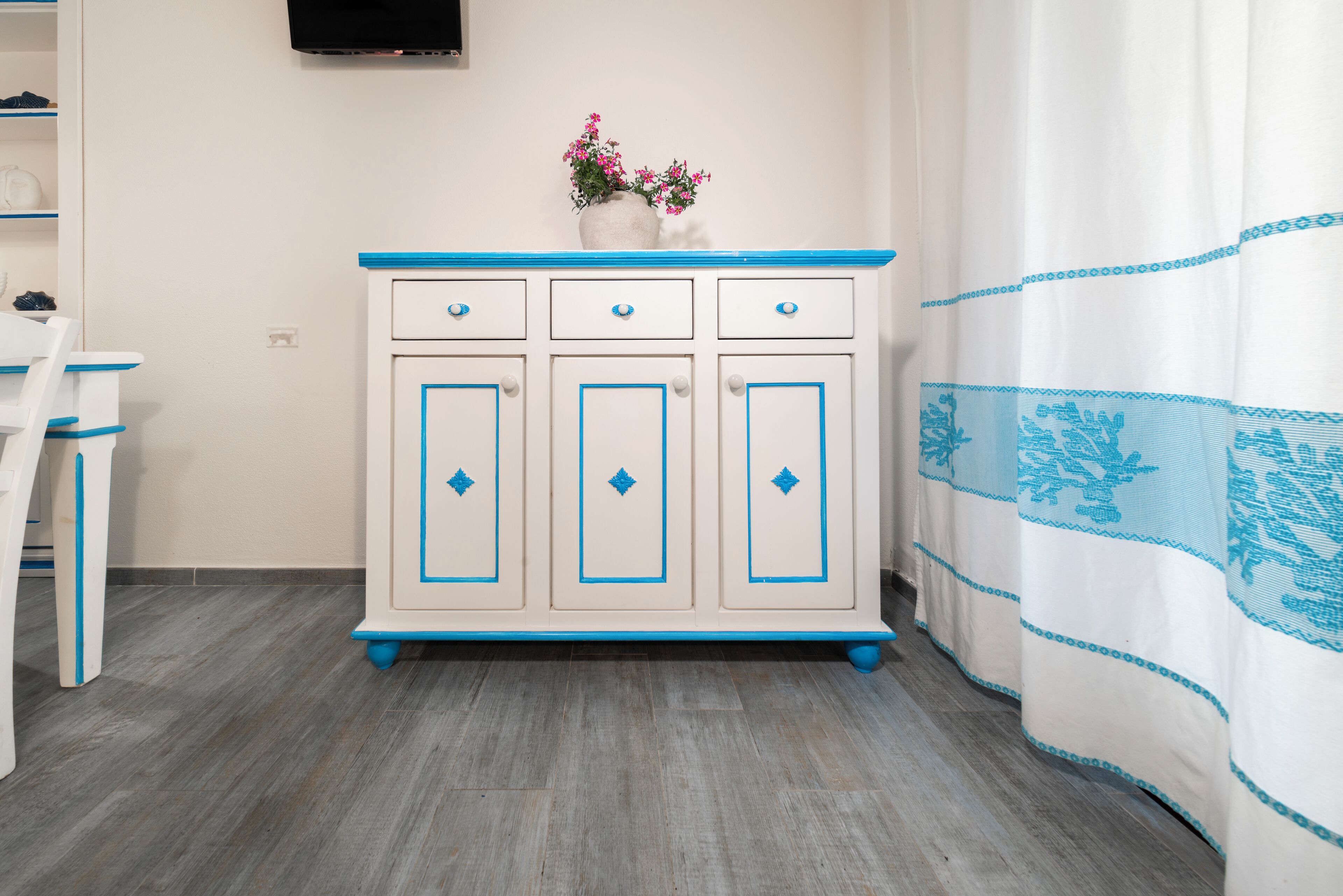 A white and blue cabinet with drawers and a vase of flowers on top.