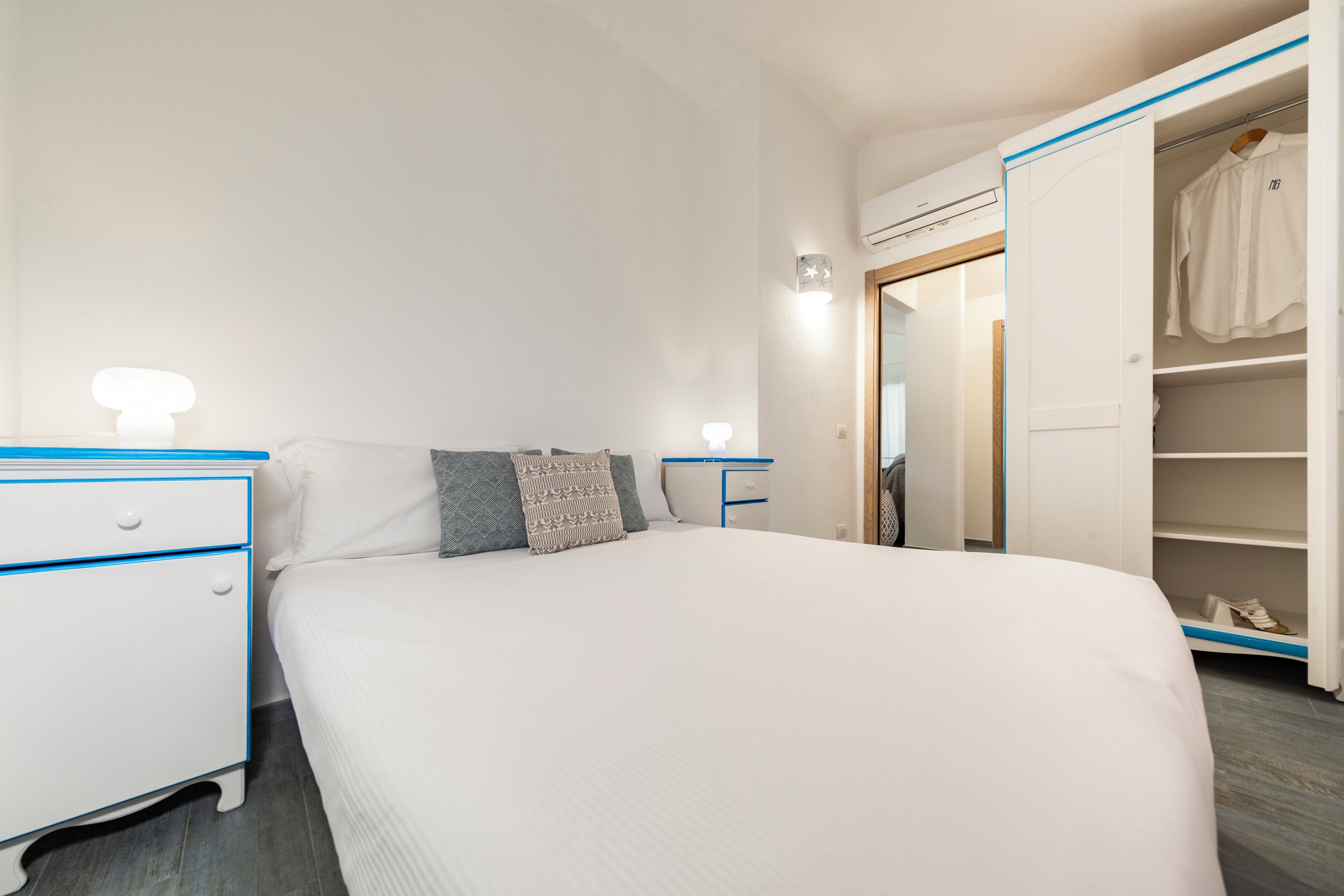 A hotel room with a large bed, a bedside table with a lamp, a wardrobe, and a mirror.