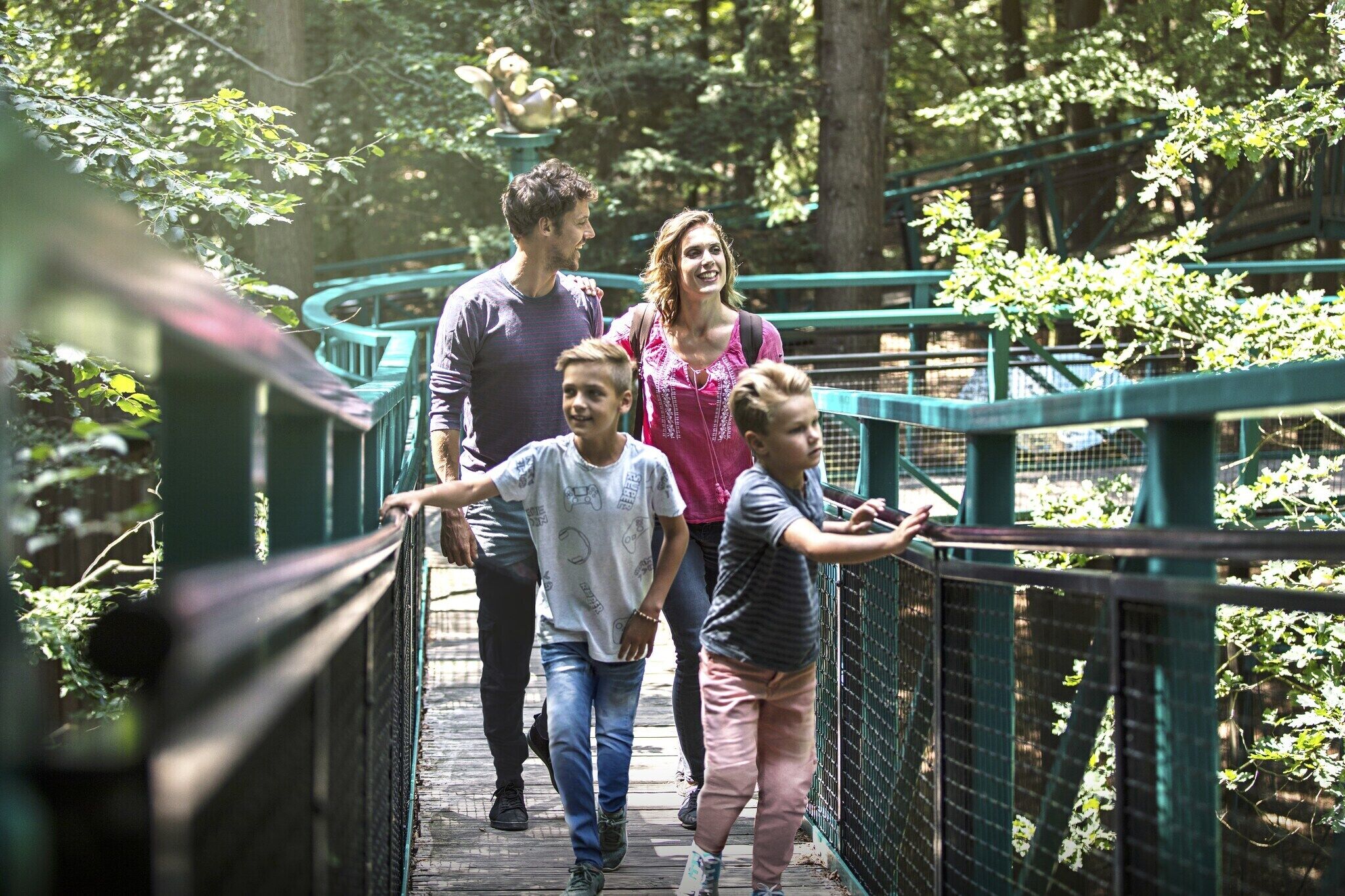 A family walking on a wooden bridge surrounded by greenery.