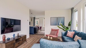 A modern living room with a blue sofa, a wooden coffee table, and a flat-screen TV mounted on the wall. - Holiday Home in Medemblik near IJsselmeer (PS Opperdoes)