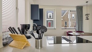 A modern kitchen with a central island, a dining area with a round table, and large windows with blinds. - Holiday Home in Medemblik near IJsselmeer (PS Opperdoes)