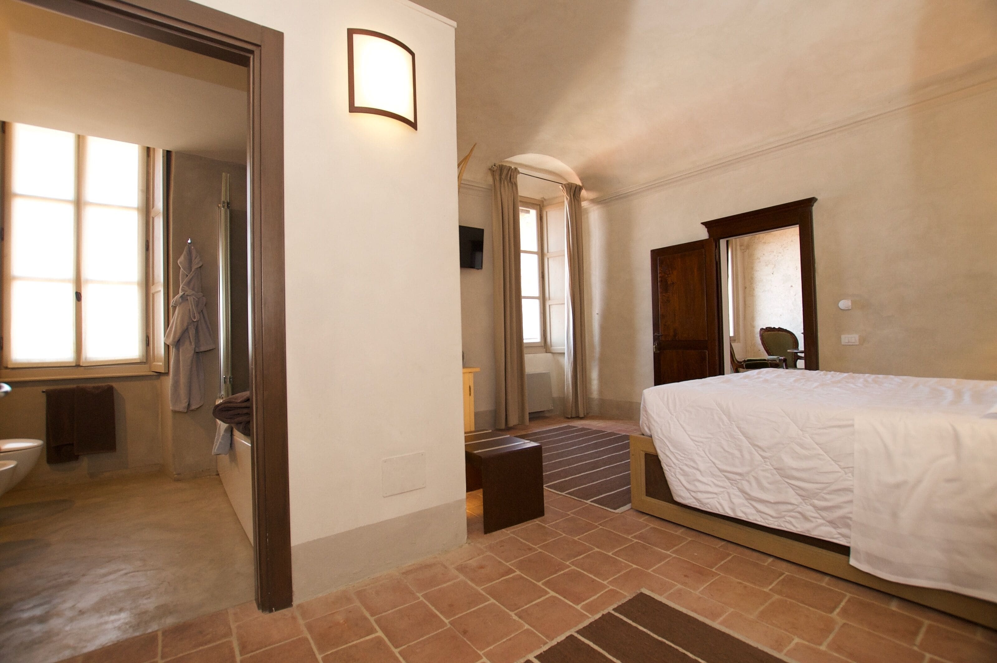 A hotel room with a bed, a bathroom, and a view of the outside.