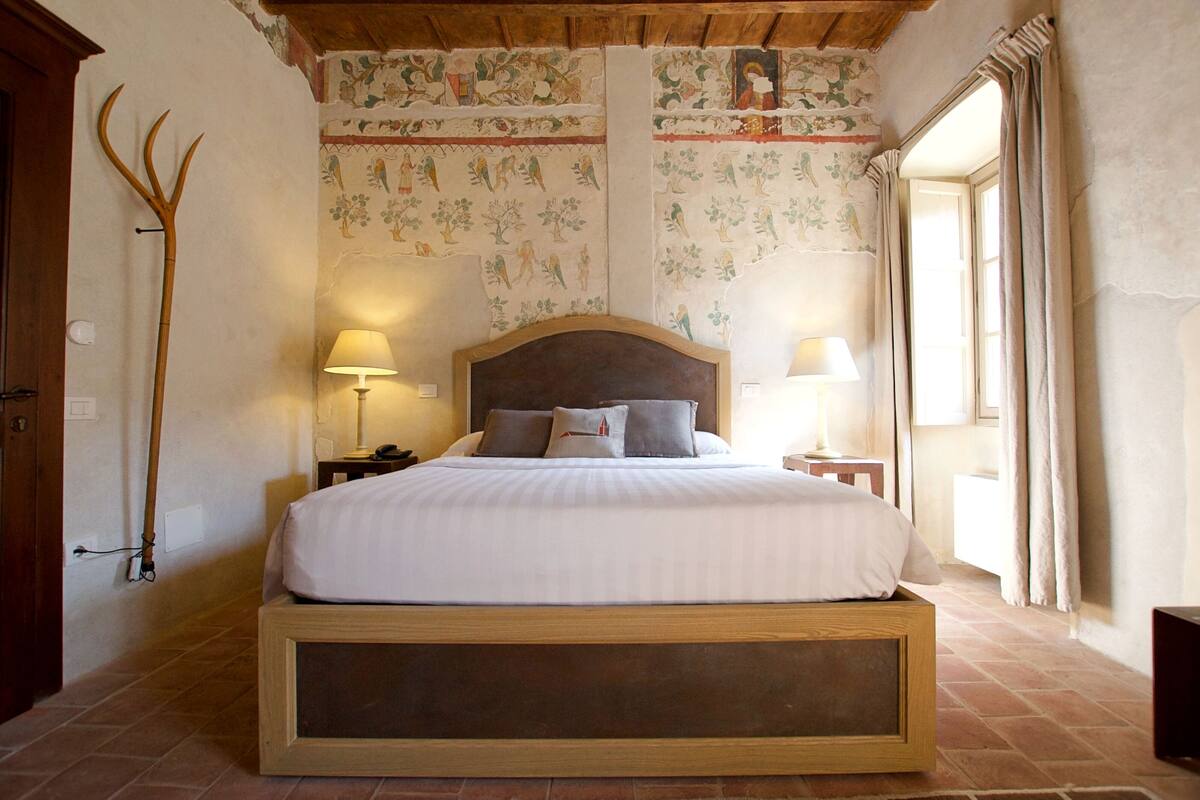 A bedroom with a large bed, two bedside lamps, a wooden headboard, and a decorative wall with floral patterns.