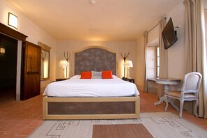 Ett hotellrum med en stor säng, två sänglampor, en tv på väggen, en stol och ett litet bord.