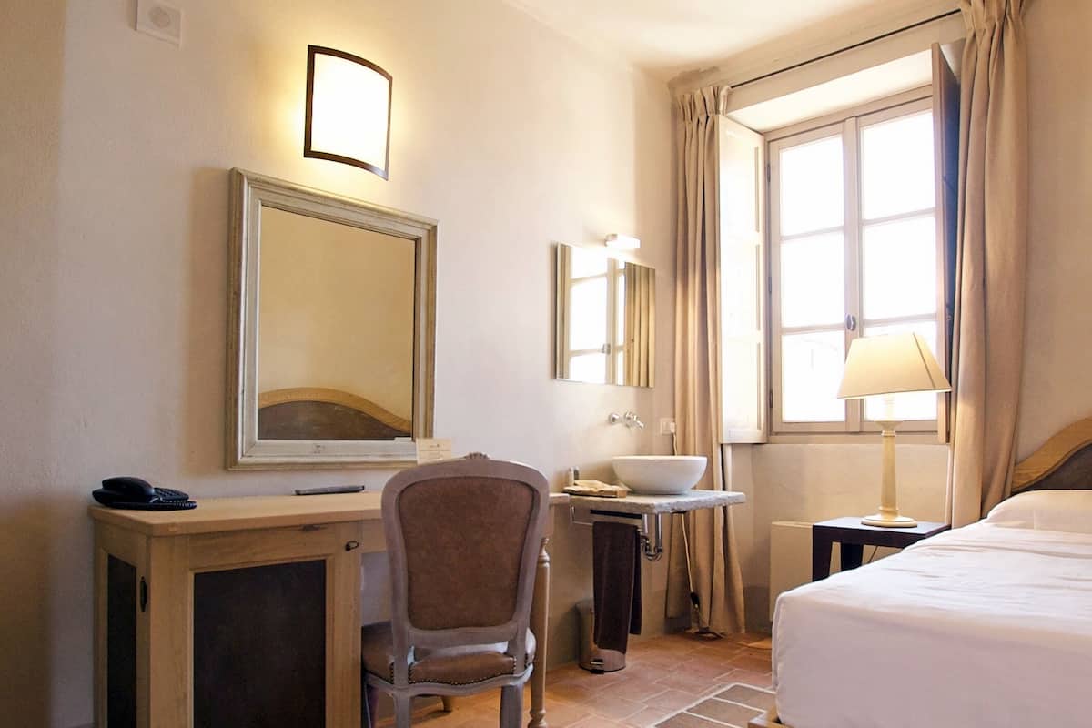 A hotel room with a bed, desk, chair, and a large window with curtains.