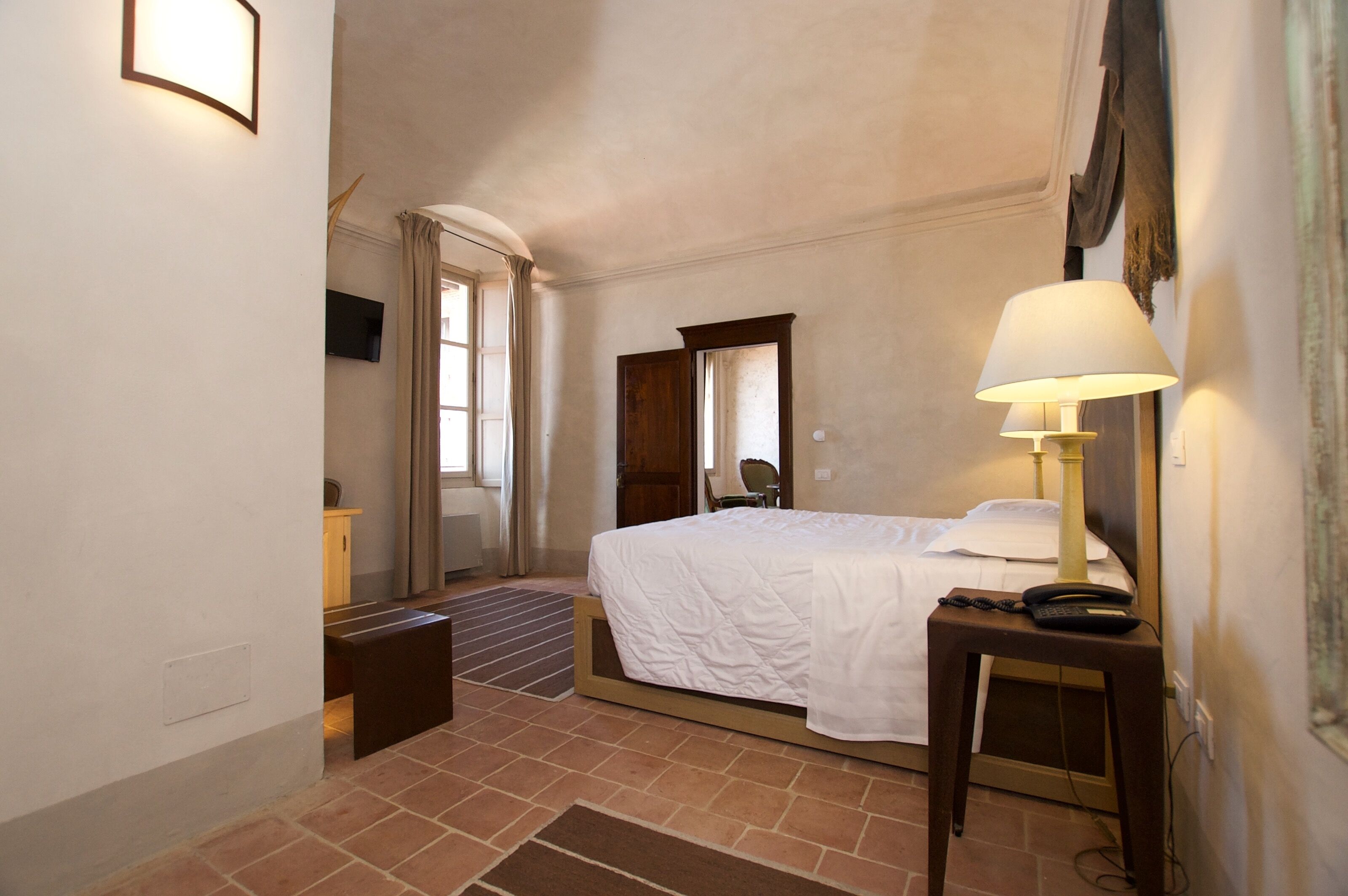 A hotel room with a bed, bedside lamp, and a small table with a phone.