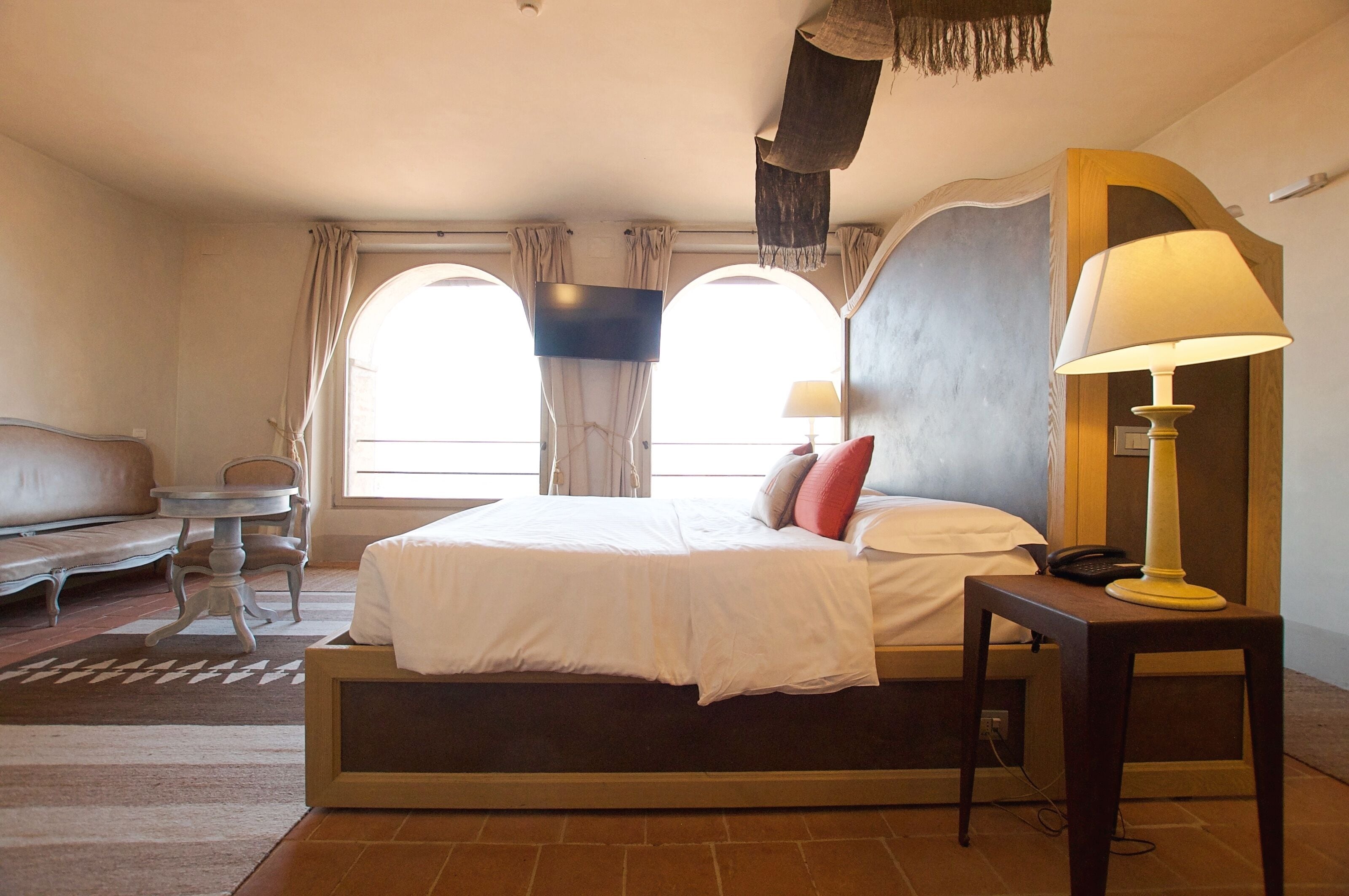 A hotel room with a bed, a bedside table with a lamp, a small table, and a sofa.