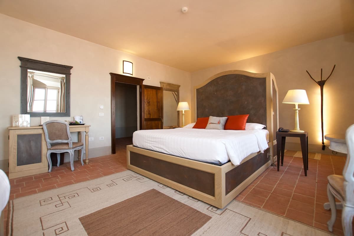 A bedroom with a large bed, a desk, a chair, a mirror, and a bedside lamp.