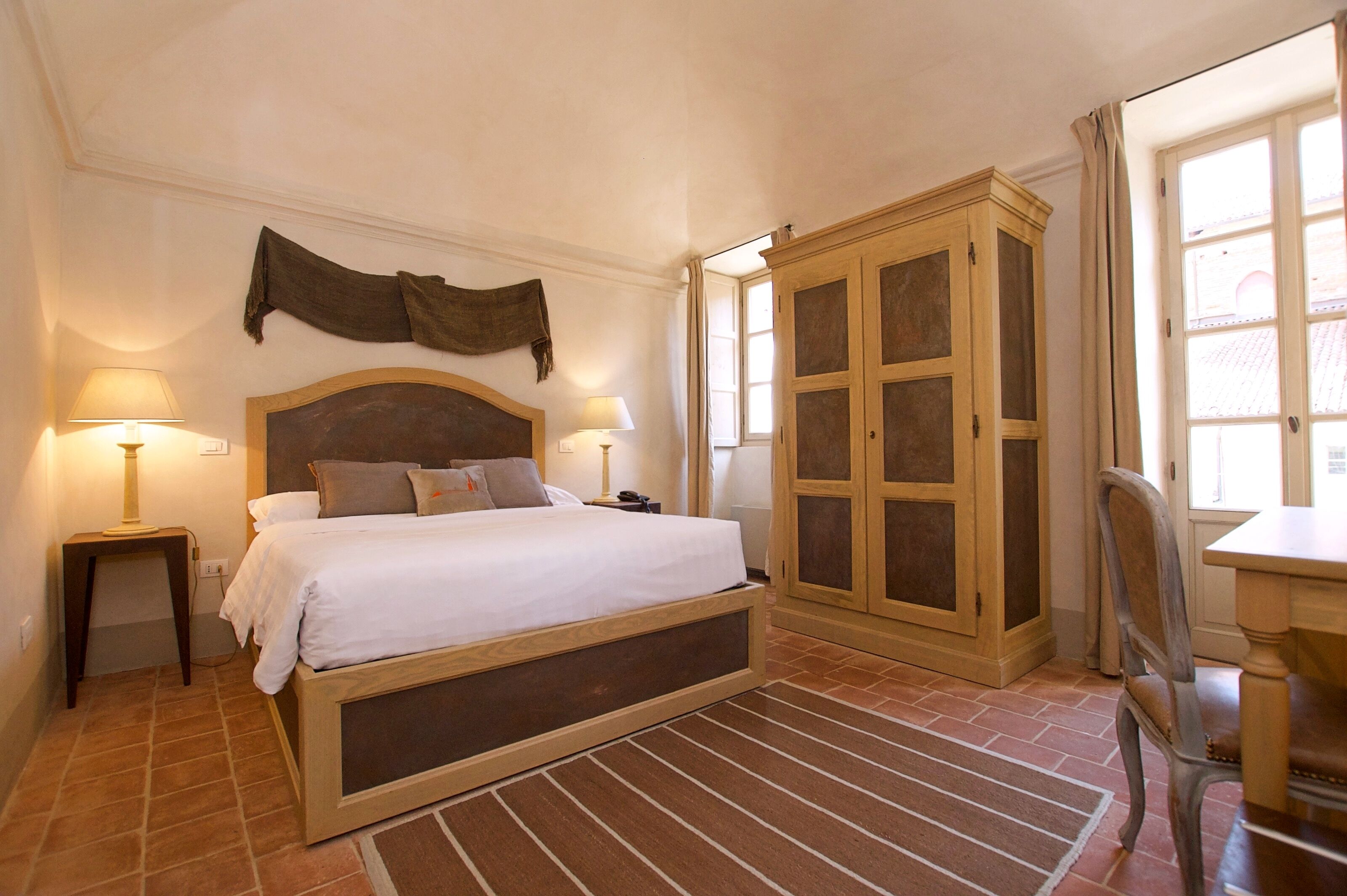 A bedroom with a large bed, two bedside lamps, a wooden wardrobe, and a window with curtains.