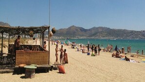 A beach with a flag, people, and a mountain in the background. - Apartment in Empuriabrava near Sandy Beach (Empuriabrava)