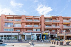 A multi-story building with balconies, storefronts including a pizzeria and a café, and outdoor seating.
