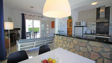Une cuisine moderne avec un mur de crédence en pierre, un coin repas doté d’une table blanche et un grand luminaire suspendu.