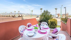A dining table set for four with white chairs, a white tablecloth, and a view of the sea and palm trees in the background.