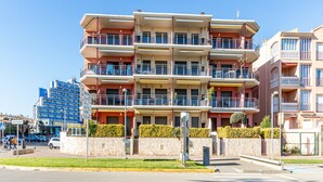 A multi-story residential building with balconies, a stone facade, and a clear blue sky.
