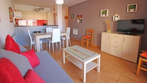 Ein Wohnzimmer mit einer Couch, einem Couchtisch, einem Fernseher und einer Küche im Hintergrund.