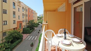 Ein Balkon mit Esstisch, der auf eine Straße mit Gebäuden und Grünflächen blickt.