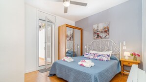 Une chambre à coucher comprenant un lit, une table de chevet, un ventilateur de plafond, une porte et une fenêtre.