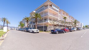 Un hôtel à plusieurs étages, doté de balcons, avec des voitures garées et des palmiers.