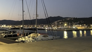 A marina at dusk with boats docked, a clear sky, and a cityscape in the background. - Apartment in Roses near de la Punta Beach (Rosas / Roses)