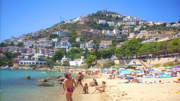 A beach with people sunbathing and swimming, surrounded by buildings on a hillside. - Apartment in Roses near de la Punta Beach (Rosas / Roses)