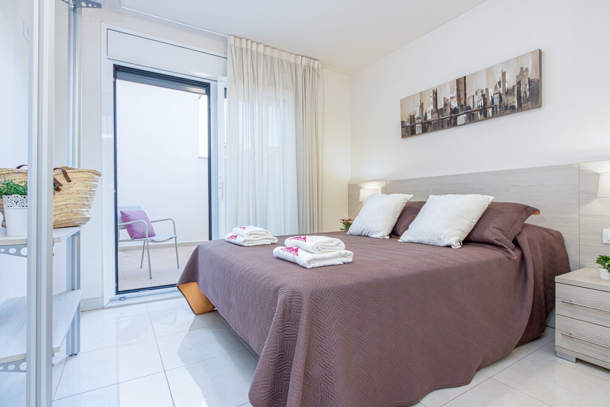 Camera d'albergo moderna con un letto grande, un dipinto con vista sulla città e una porta scorrevole in vetro che dà su un balcone.