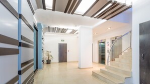 Un hall d’hôtel moderne avec un escalier central, un comptoir d’accueil et une plante en pot.