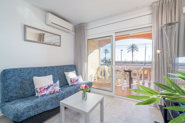 A modern living room with a blue sofa, a white coffee table, and a view of an outdoor patio with a table and chairs.