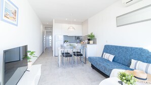 Een moderne woonruimte met een bank, televisie, eethoek, keuken en een gang die naar een andere kamer leidt.