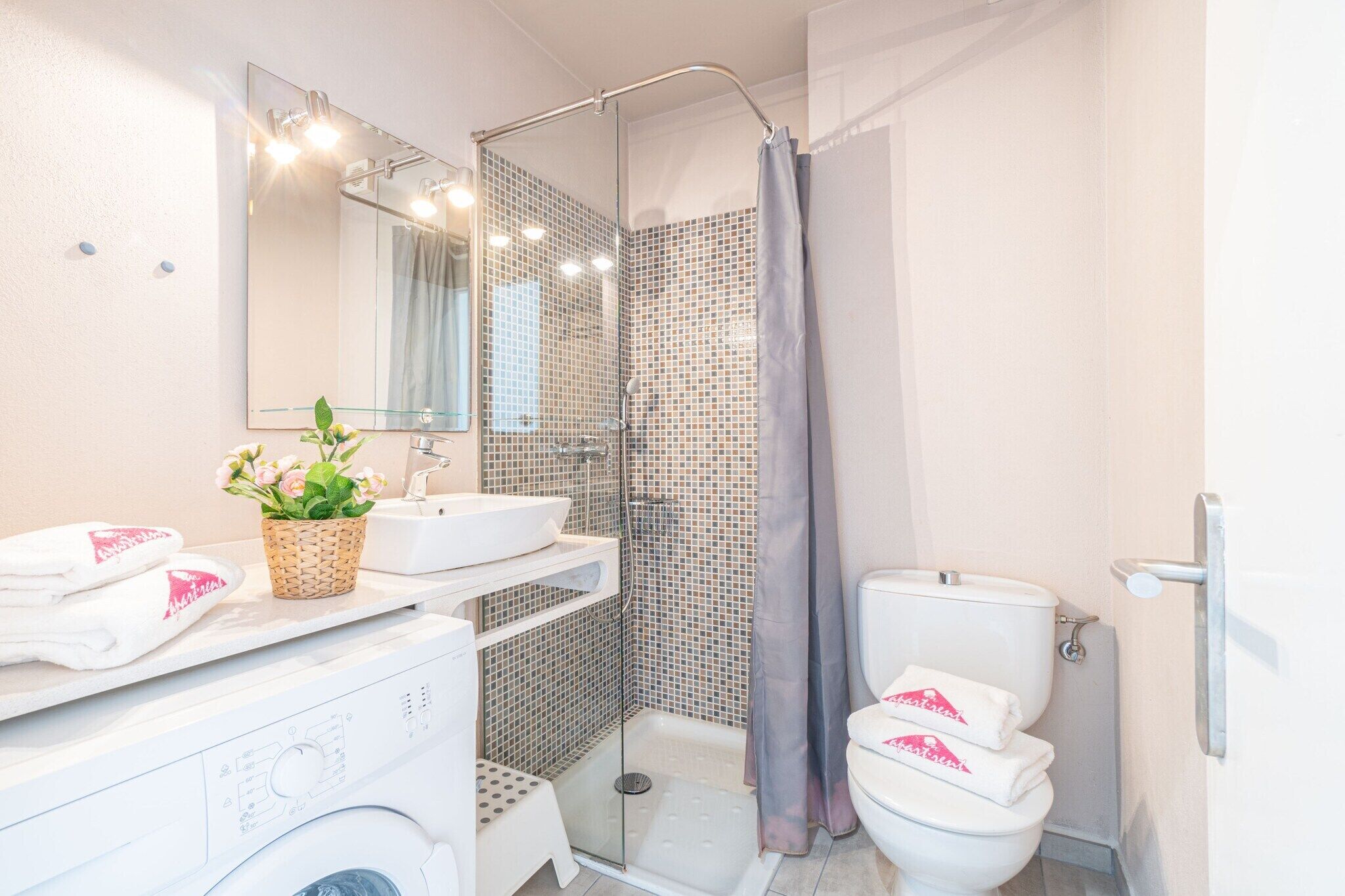 A bathroom with a glass shower enclosure, a white sink, a toilet, and a washing machine.