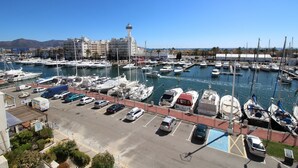 Ein Yachthafen mit vertäuten Booten, ein Leuchtturm und ein Parkplatz mit Autos.