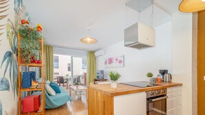 Cocina compacta con encimera de madera, horno integrado y un pequeño comedor con una silla y una mesa.