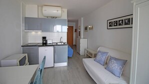 A compact living space with a kitchenette, a white sofa with patterned cushions, and a small dining table. - Studio in Empuriabrava with Ocean Views (Empuriabrava)