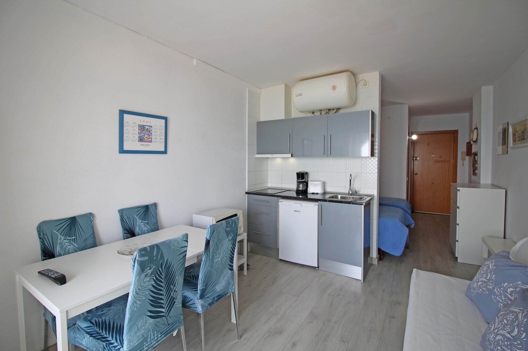 Ein kleines Hotelzimmer mit Küchenzeile, Essbereich mit Stühlen, einem Bett und einem Badezimmer.