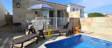 A swimming pool with lounge chairs and a table, a covered seating area, and a stone wall.