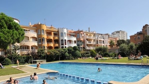 A swimming pool surrounded by multi-story buildings with balconies, a grassy area, and people relaxing. - Apartment in Empuriabrava by the Beach (Empuriabrava)