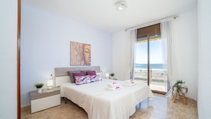 A bedroom with a bed, nightstands, a painting, a window with a view, and a small plant stand. - Apartment in Empuriabrava by the Beach (Empuriabrava)