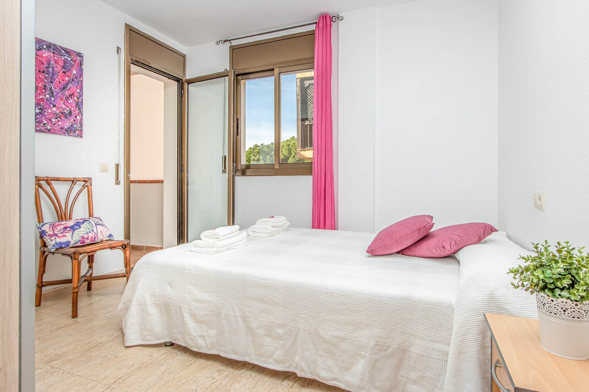 A bedroom with a bed, a chair, a window with curtains, and a potted plant.