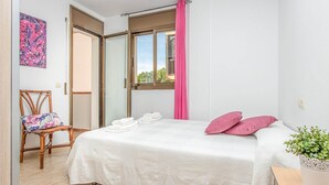 A bedroom with a bed, a chair, a window with curtains, and a potted plant. - Apartment in Empuriabrava by the Beach (Empuriabrava)