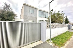 A modern two-story house with a grey exterior, a metal fence, and a small garden area. - Villa in Empuriabrava with Private Pool (Empuriabrava)