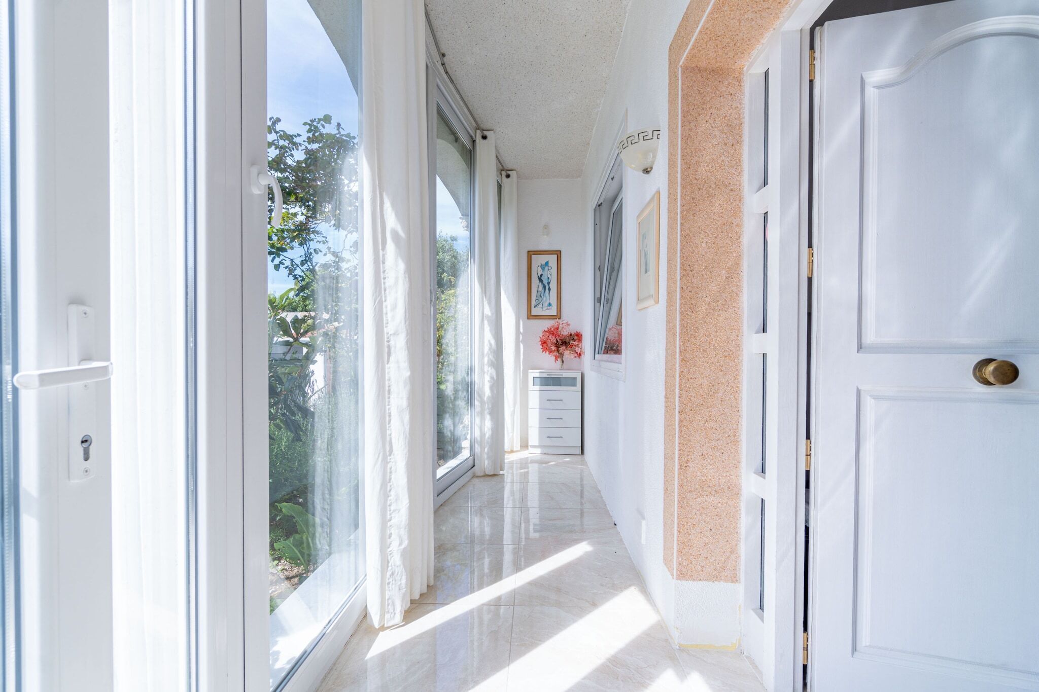 A hallway with a white door, a framed picture, and a small table with a vase of flowers.