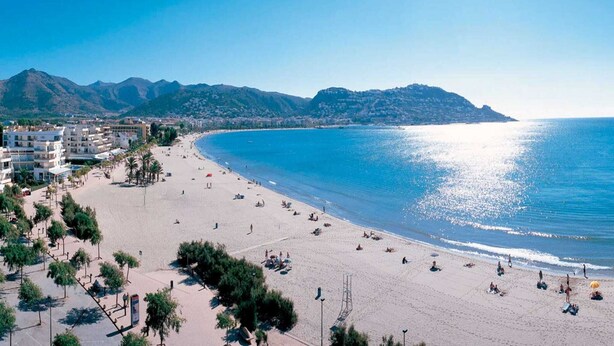 A beach with clear blue water, a sandy shore, and a mountainous backdrop. - Apartment in Roses near the Beach (Rosas / Roses)