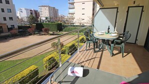 A balcony with a table set for two, a chair, and a small garden area with hedges and a bench. - Apartment in Roses near the Beach (Rosas / Roses)