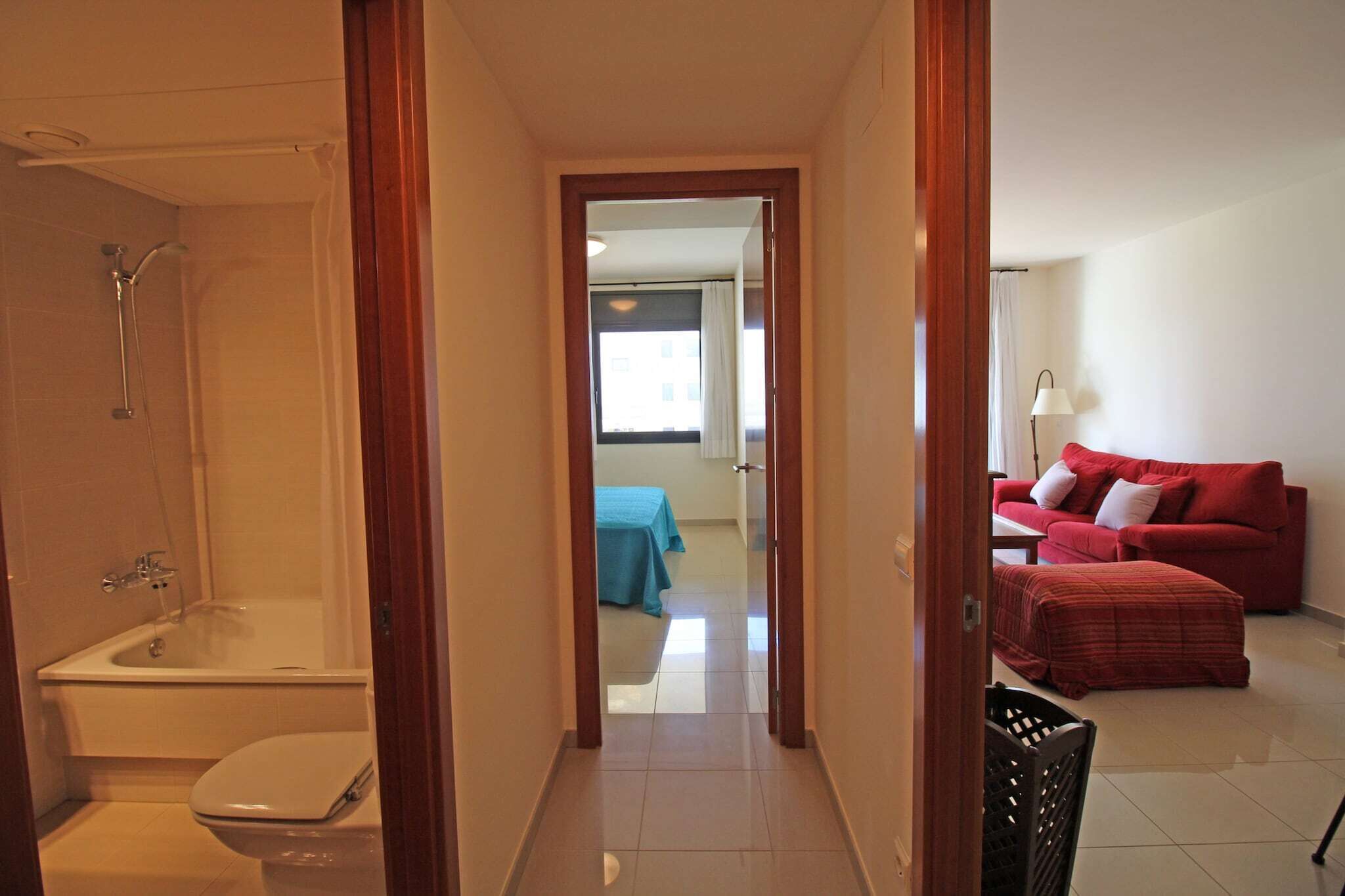 A hotel room with a bathroom, a red sofa, and a bed with a blue bedspread.